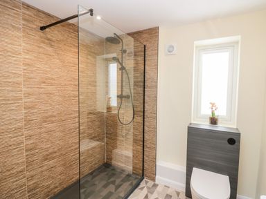A bathroom with a walk in shower with glass panel tiled walls and a toilet under a window at How Hill Farm Cottage in Greystoke