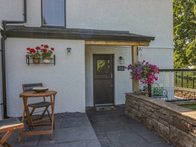 An outdoor patio with a wooden table and chairs flower pots on the wall and a door at How Hill Farm Cottage in Greystoke