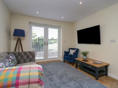 A living room with a sofa a blue armchair a coffee table a floor lamp and a wall-mounted TV at How Hill Farm Cottage Greystoke