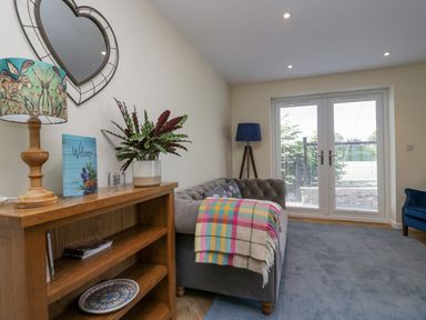 A living room with a wooden bookshelf a sofa with a colorful blanket and glass doors at How Hill Farm Cottage in Greystoke