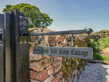 A metal sign pointing left attached to a stone wall with greenery and a tree in the background at How Hill Farm Cottage Greystoke