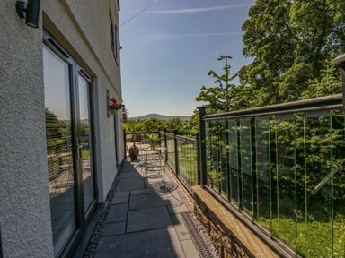 A balcony with metal chairs and tables outside a building with glass railings and trees in the background at How Hill Farm Cottage in Greystoke