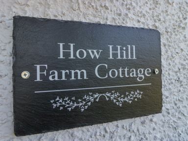 A black plaque with white text reading How Hill Farm Cottage on a textured white wall at How Hill Farm Cottage in Greystoke
