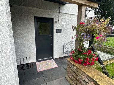 A door with a doormat and flowers at How Hill Farm Cottage in Greystoke