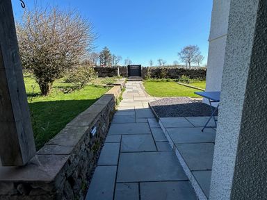 A garden view with a pathway, stone wall, and gate at How Hill Farm Cottage in Greystoke