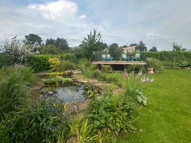 A garden with a pond and a deck with chairs at How Hill Farm Cottage Greystoke