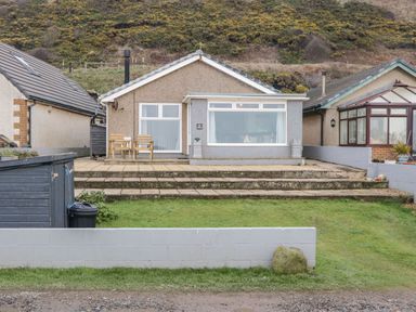 A bungalow with patio chairs and steps leading to a grass garden at The Chalet in Coulderton near Egremont Cumbria