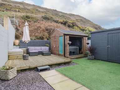 An outdoor patio with a wooden deck sofa set umbrella shed and artificial grass at The Chalet in Coulderton near Egremont Cumbria