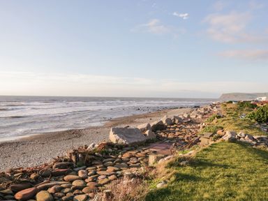A rocky beach with waves and grass next to a pathway made of large rounded stones at The Chalet in Coulderton near Egremont Cumbria