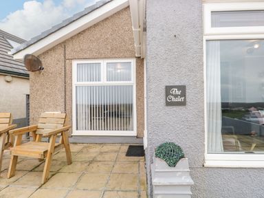 The exterior of a house with wooden chairs on a tiled patio and a sign that reads The Chalet at The Chalet in Coulderton near Egremont Cumbria