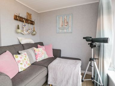 A gray sofa with floral and pink cushions next to a telescope on a tripod by a window with curtains at The Chalet in Coulderton near Egremont Cumbria