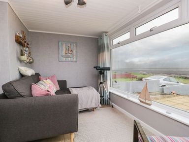 A sitting area with a gray sofa pink cushions a telescope and a small wooden sailboat on the window at The Chalet in Coulderton near Egremont Cumbria