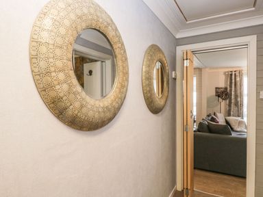 A hallway with two round decorative mirrors on the wall and a view into a living room with a sofa at The Chalet in Coulderton near Egremont Cumbria