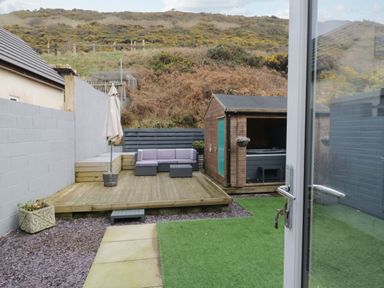 A backyard with a wooden deck seating area a wooden shed and artificial grass at The Chalet in Coulderton near Egremont Cumbria