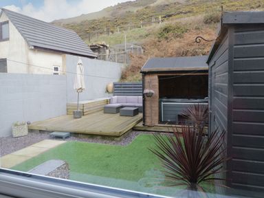 A backyard with a wooden deck seating area hot tub shed and artificial grass at The Chalet in Coulderton near Egremont Cumbria