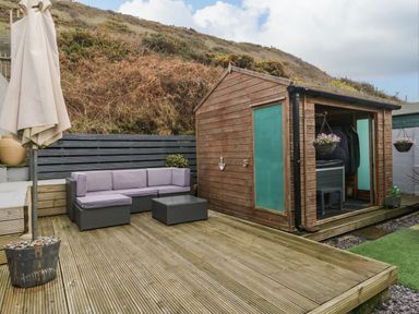A wooden deck with patio furniture and a wooden shed near a hillside at The Chalet in Coulderton near Egremont Cumbria