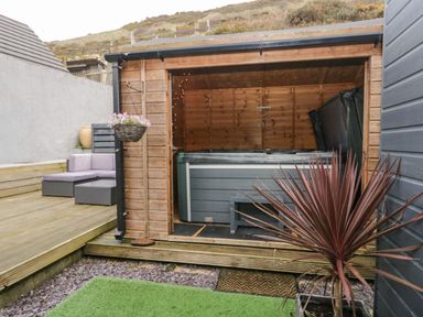 A wooden outdoor structure with a hot tub inside and cushioned seating on a wooden deck at The Chalet in Coulderton near Egremont Cumbria