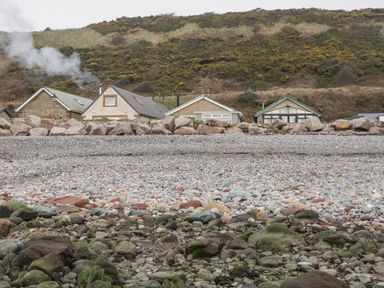 A pebble beach with rocks in front of houses and a hillside at The Chalet in Coulderton near Egremont Cumbria