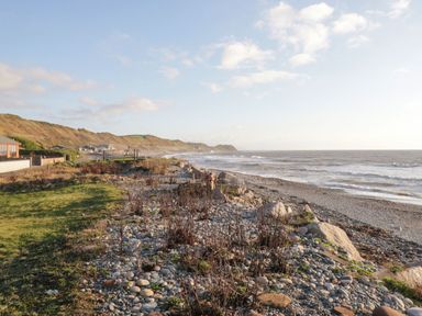 A rocky beach with pebbles and sparse vegetation next to the sea and hills with houses in the distance at The Chalet in Coulderton near Egremont Cumbria