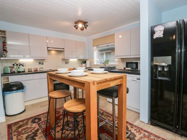 A kitchen with a wooden dining table and stools a black refrigerator and white cabinets at The Chalet in Coulderton near Egremont Cumbria