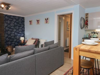 A living room with gray sofas a wooden dining table with bowls and plates and an open doorway at The Chalet in Coulderton near Egremont Cumbria