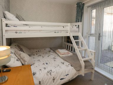 A bedroom with a white bunk bed next to glass doors and a wooden nightstand with a lamp at The Chalet in Coulderton near Egremont Cumbria