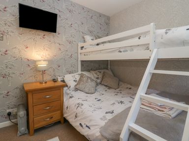 A bedroom with a bunk bed wooden nightstand with a lamp and a wall mounted television at The Chalet in Coulderton near Egremont Cumbria