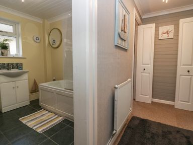 A bathroom with a bathtub a sink and a striped mat next to a hallway with a radiator and two white doors at The Chalet in Coulderton near Egremont Cumbria