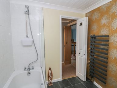 A bathroom with a bathtub and shower head a towel radiator and an open door showing an adjoining room at The Chalet in Coulderton near Egremont Cumbria