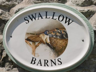 An oval sign on a stone wall with birds and nest illustration and text swallow barns