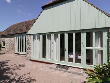 Exterior of a stone building with multiple light green framed glass doors and windows at Swallow Barns in Chipping Sodbury