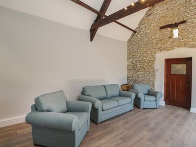 A living room with blue sofa and chairs wooden floor stone wall with door and exposed ceiling beams at Swallow Barns in Chipping Sodbury