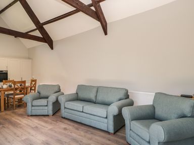 A living room with three grey upholstered armchairs and a sofa with a wooden dining table and chairs in the background at Swallow Barns in Chipping Sodbury