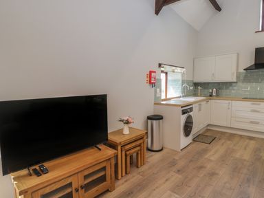 A kitchen and living area with a television on a wooden stand and nested tables with flowers at Swallow Barns in Chipping Sodbury