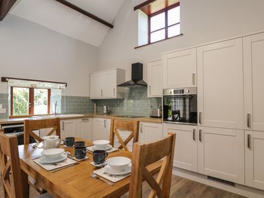 A kitchen with wooden dining table and chairs set with dishes and mugs and white cabinets at Swallow Barns in Chipping Sodbury