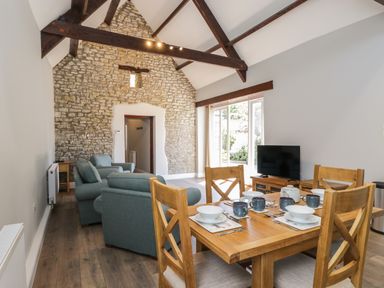 A dining table set with dishes and mugs in a living area with sofas a stone wall and a TV at Swallow Barns in Chipping Sodbury