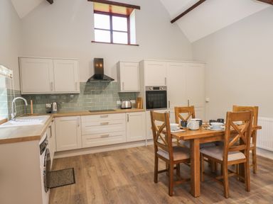 A kitchen with wooden dining table and chairs and white cabinets at Swallow Barns in Chipping Sodbury