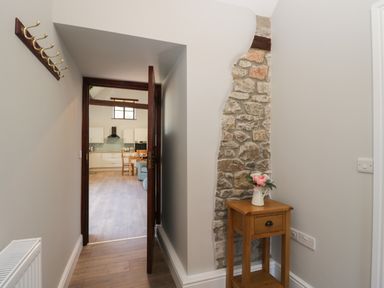 A hallway with wooden floor a small table with flowers and exposed stonework leading to a kitchen with wooden dining table at Swallow Barns in Chipping Sodbury
