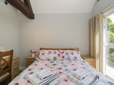 A bedroom with a double bed floral bedding wooden bedside tables and a window with curtains at Swallow Barns in Chipping Sodbury