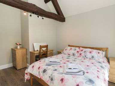 A bedroom with a wooden bed and floral bedding a wooden wardrobe a dressing table with a chair and a small chest of drawers at Swallow Barns in Chipping Sodbury