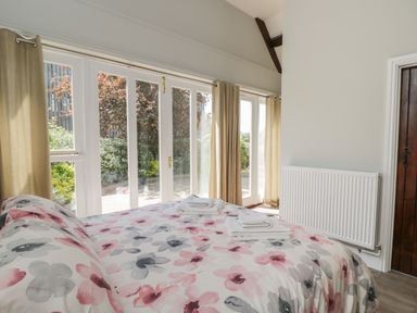 A bedroom with a floral bedspread towels on the bed large windows with curtains and a wooden door at Swallow Barns in Chipping Sodbury