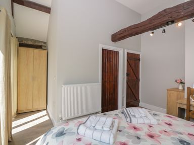 A bedroom with a floral bedspread, wooden wardrobe, wooden doors, radiator, and wooden beam at Swallow Barns in Chipping Sodbury