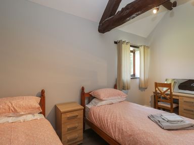 A bedroom with two single beds a wooden nightstand between them a window with curtains and a wooden desk with a chair at Swallow Barns in Chipping Sodbury