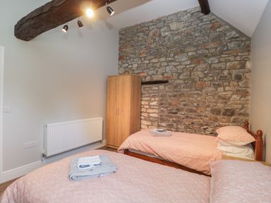 A bedroom with two beds pink bedding a wooden wardrobe and a stone feature wall at Swallow Barns in Chipping Sodbury