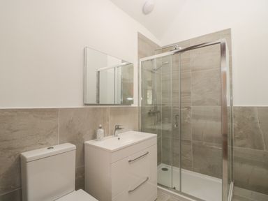 A bathroom with a toilet, a sink vanity with a mirror above it, and a glass enclosed shower at Swallow Barns in Chipping Sodbury