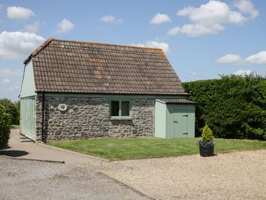 A stone house with a tiled roof next to a driveway and a hedge at Swallow Barns in Chipping Sodbury