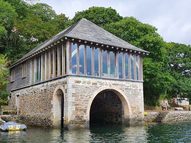 A stone boathouse with wooden upper level and large windows by water at Oakenhurst in Golant