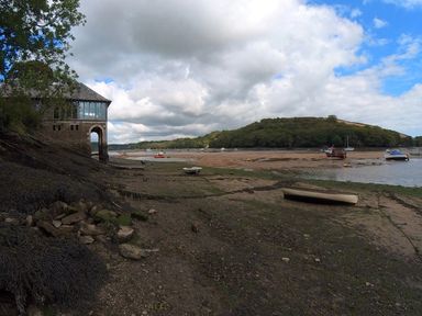 A riverside scene with boats on mudflats and a stone building on the left at Oakenhurst in Golant