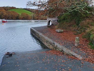 A riverside area with boats on water stone wall fallen leaves and a small stone building at Oakenhurst in Golant