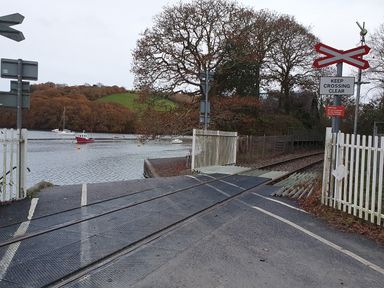 A railway crossing near water with boats and trees at Oakenhurst in Golant